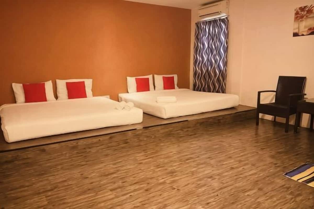 Ein Hotelzimmer mit zwei Betten, Holzboden, einem Stuhl und einem Vorhang.