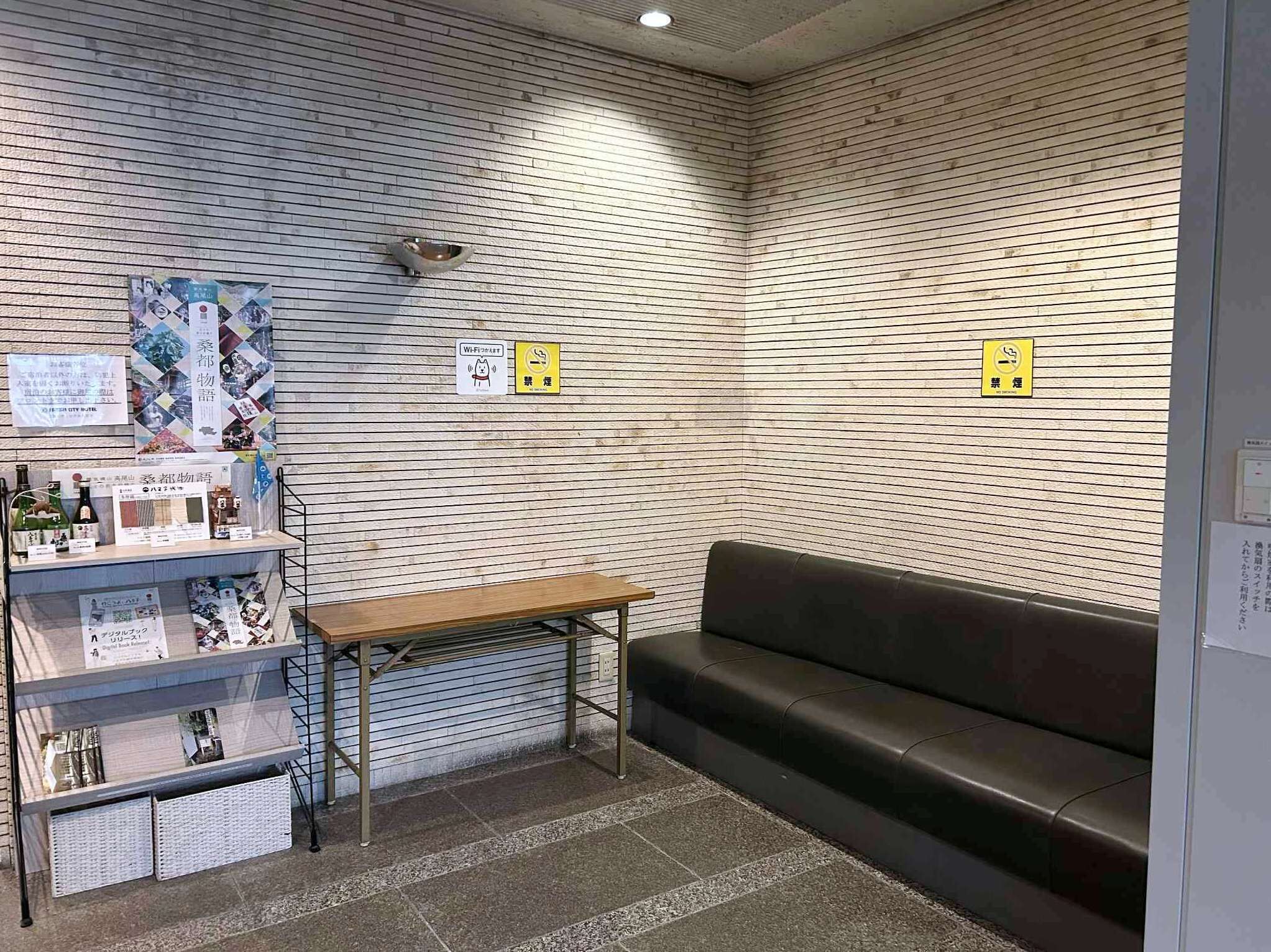 Une salle d’attente équipée d’un banc en bois, d’un canapé en cuir noir et d’une petite table sur laquelle sont disposées des brochures.
