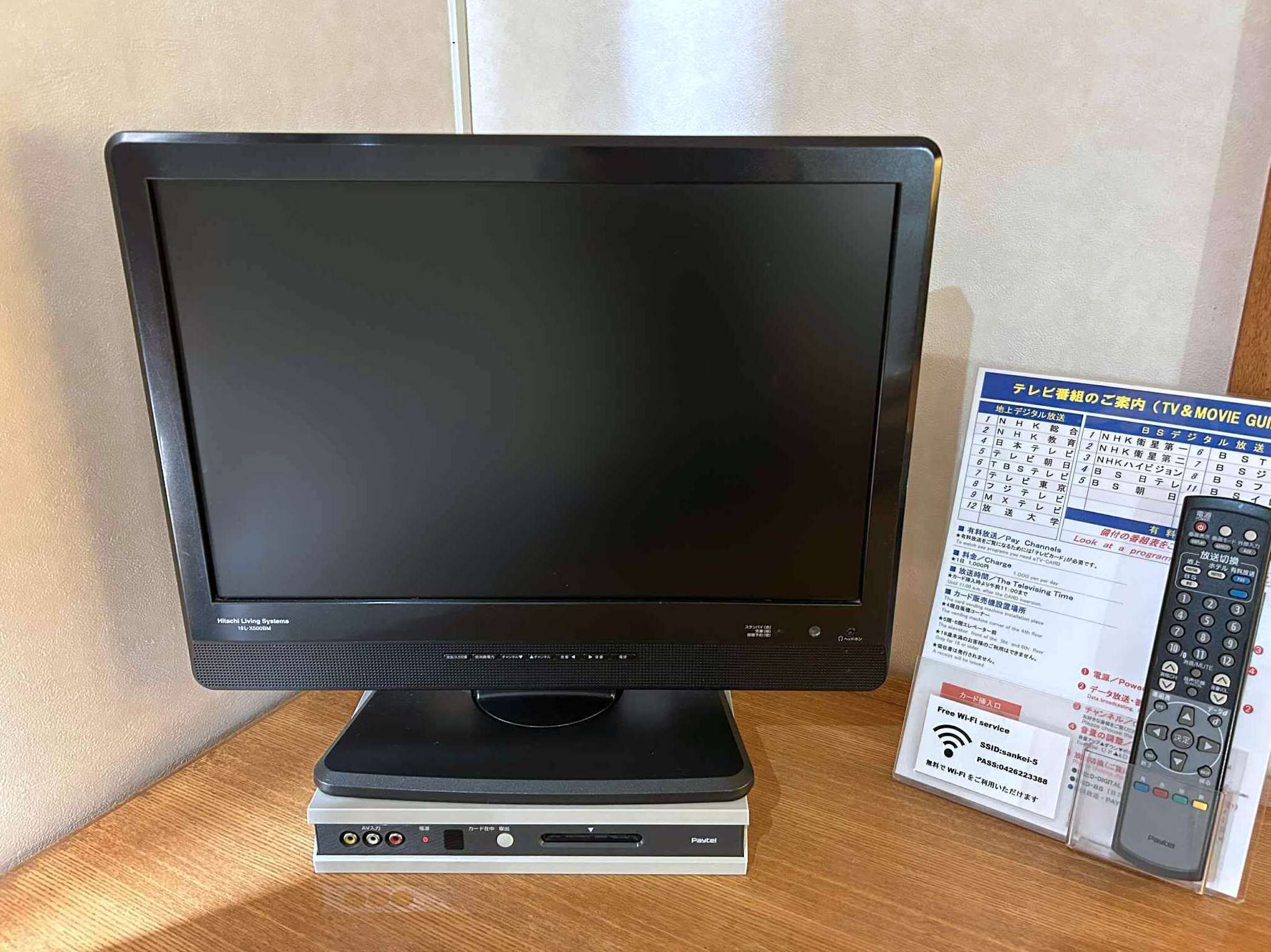 A television with a remote control and a user manual on a wooden table.