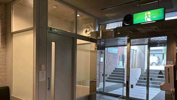 A hotel entrance with a glass door, a green emergency exit sign, and a staircase leading outside. - Sankei City Hotel Hachiouji (Hachioji)