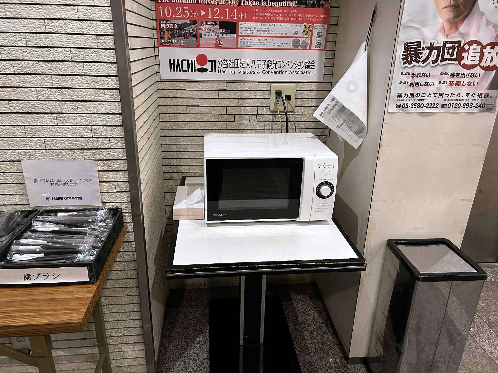 A hotel room with a white microwave on a table, a sign for the Sansei City Hotel, and a poster on the wall.