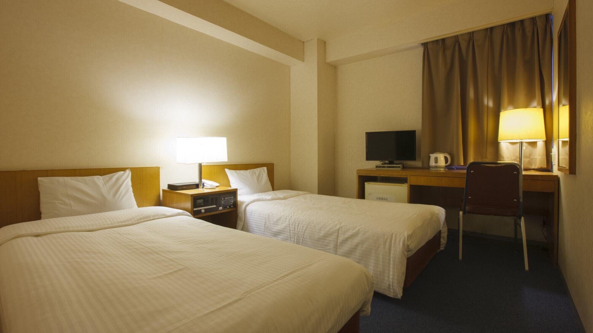Een hotelkamer met twee bedden, een bureau, een stoel, een televisie en een lamp.
