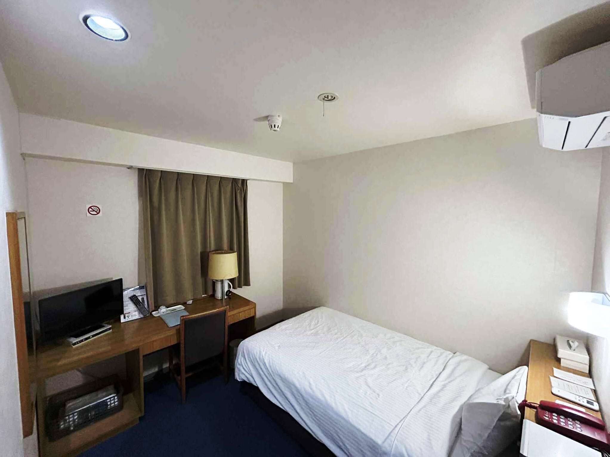 A hotel room with a bed, a desk with a computer, a television, a lamp, and a telephone.