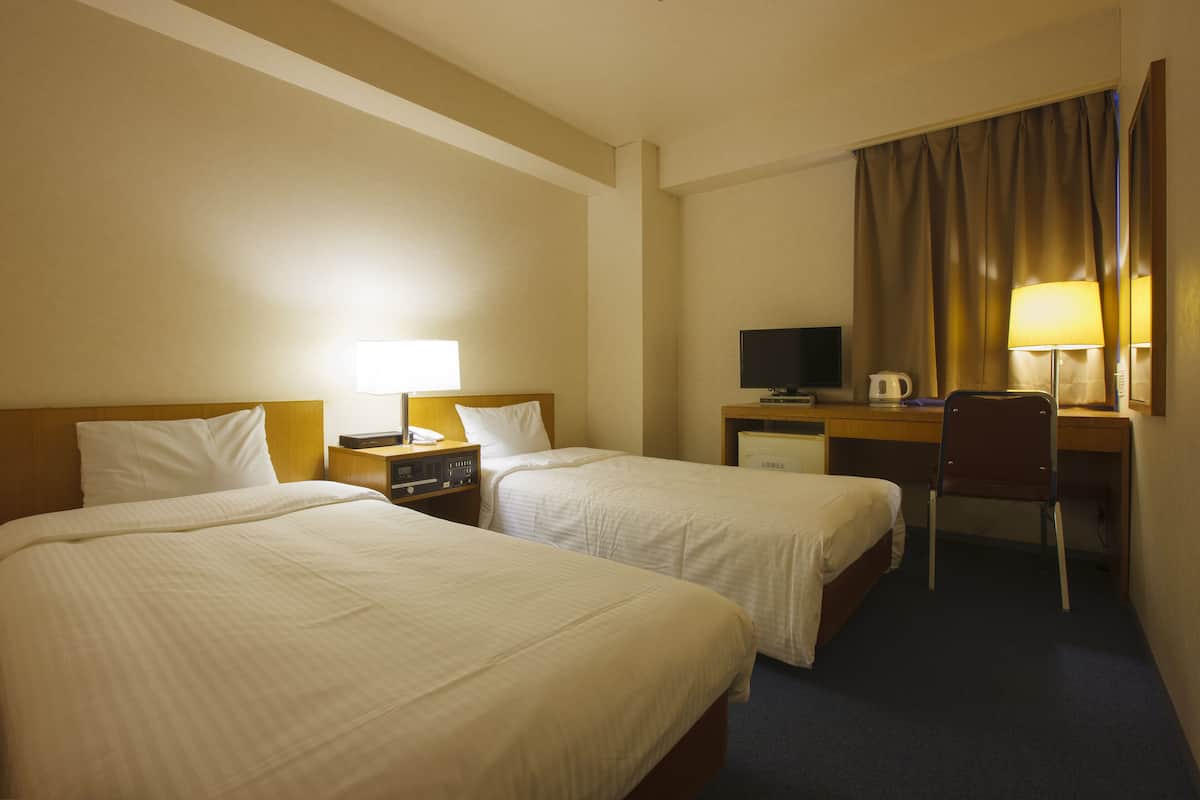 A hotel room with two beds, a desk with a computer, a chair, and a television.