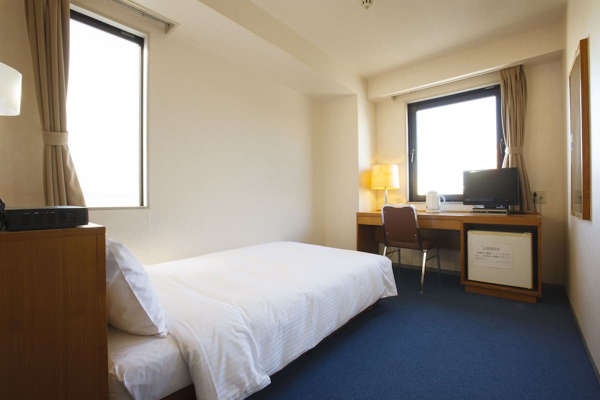 A hotel room with a single bed, a desk with a computer and lamp, and a small cabinet.
