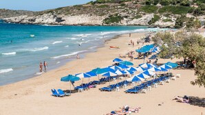 Ein Strand mit Reihen blauer und weißer Sonnenschirme, Sandstrand und ein Gebäude auf einem Hügel im Hintergrund.