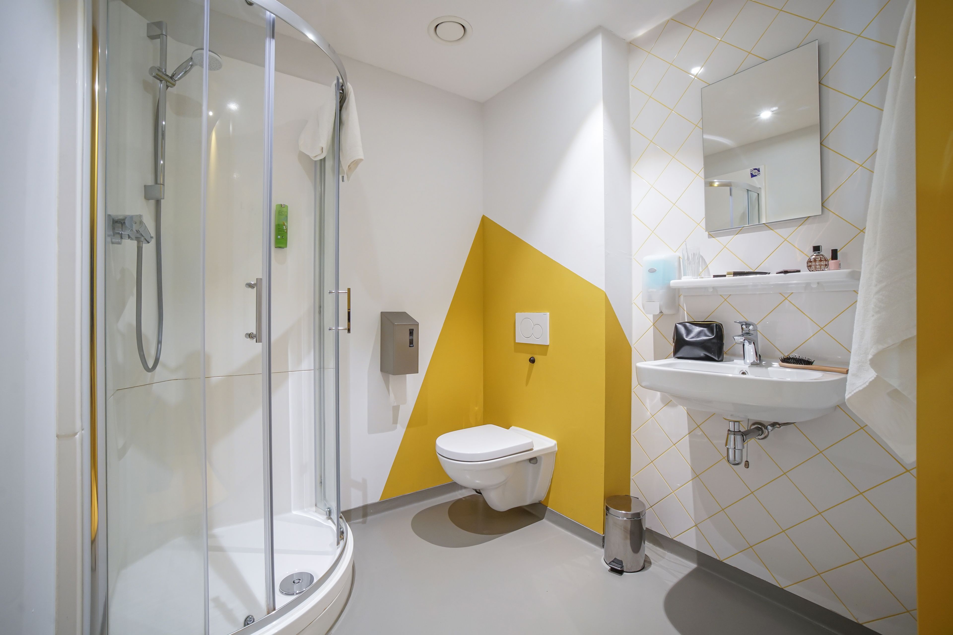 Un baño moderno con ducha envuelta en vidrio, lavamanos blanco y una pared de acento amarilla.