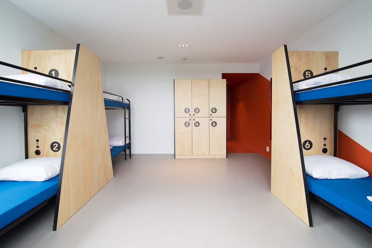 A dormitory room with bunk beds, a wardrobe, and a door.