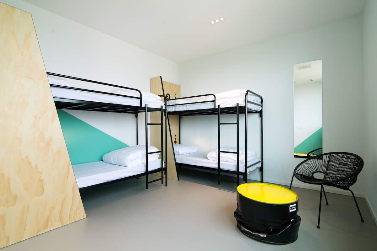 A dormitory room with bunk beds, a black chair, and a yellow bucket.