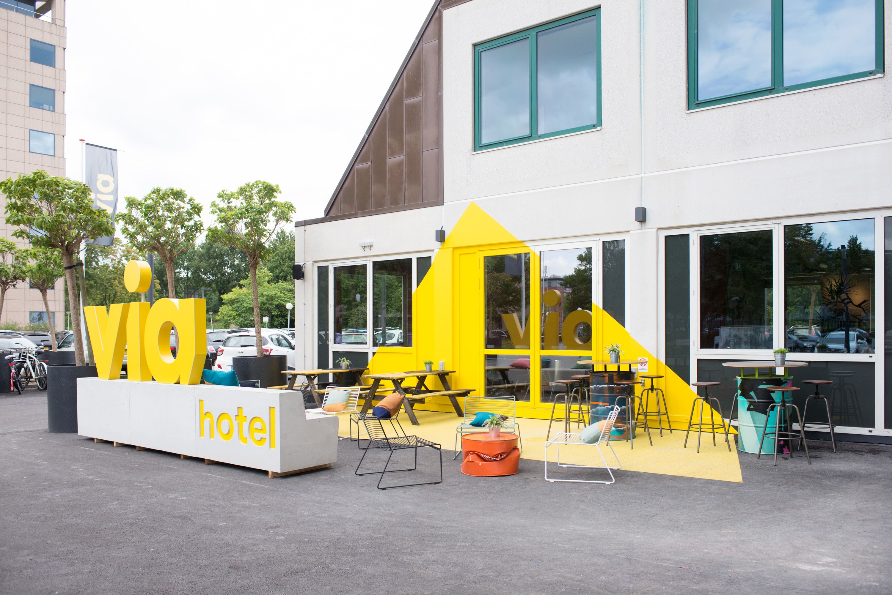 Un hotel moderno con una decoración amarillo y blanco, zona de estar al aire libre y entrada visible.