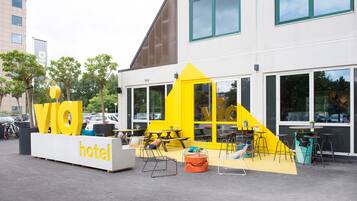 Un hotel moderno con una decoración amarillo y blanco, zona de estar al aire libre y entrada visible.