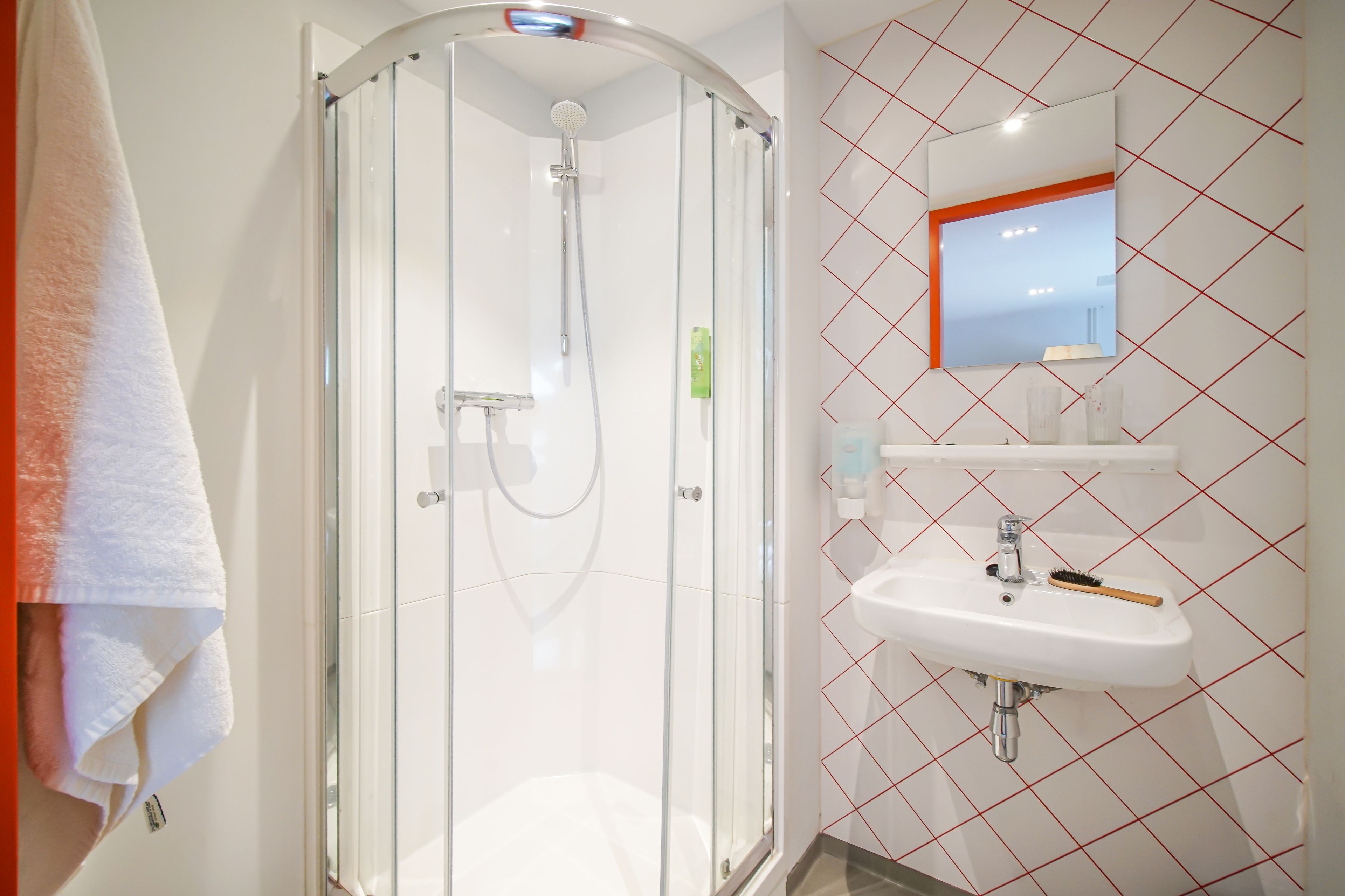 A bathroom with a glass-enclosed shower, a white sink with a mirror above it, and a towel hanging on the wall.