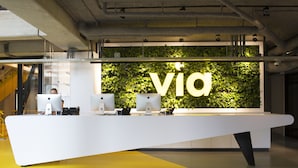 A reception desk with a 'via' sign, multiple monitors, and a green wall. - Via Amsterdam - Hostel (Diemen)