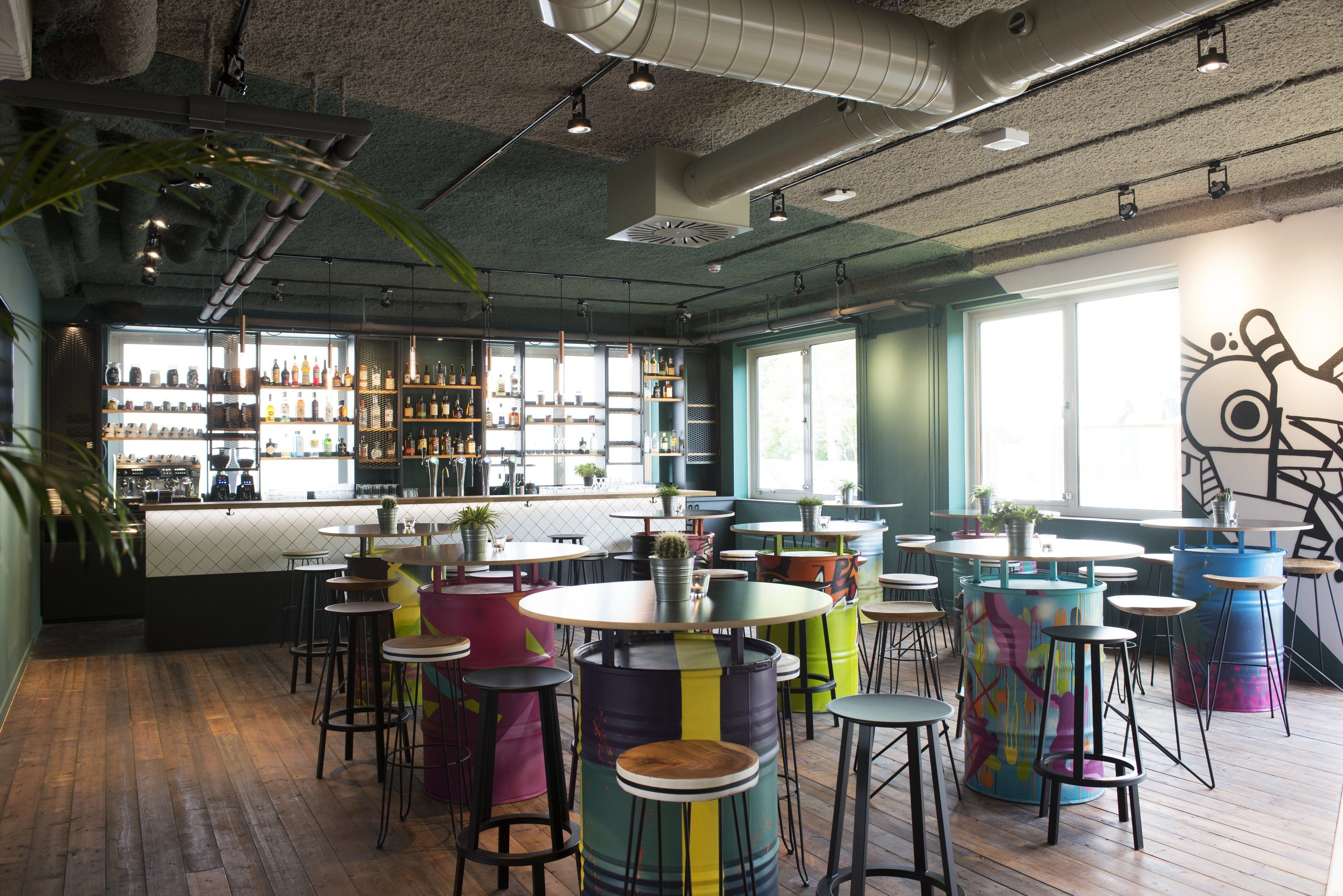 A restaurant interior with wooden floors, round tables, colorful stools, and a bar area with shelves of bottles.