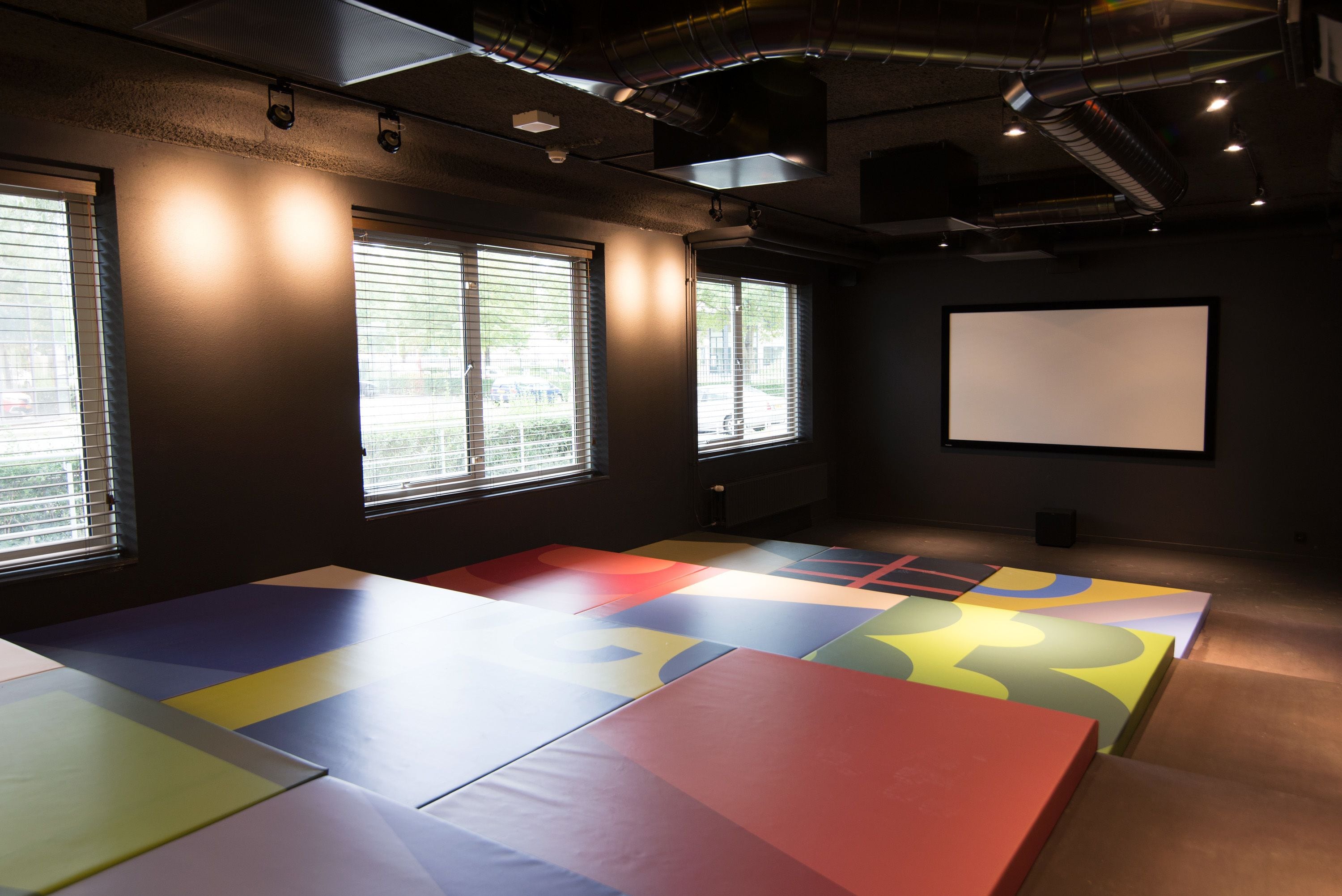 A conference room with large windows, a projector screen, and colorful padded floor mats.