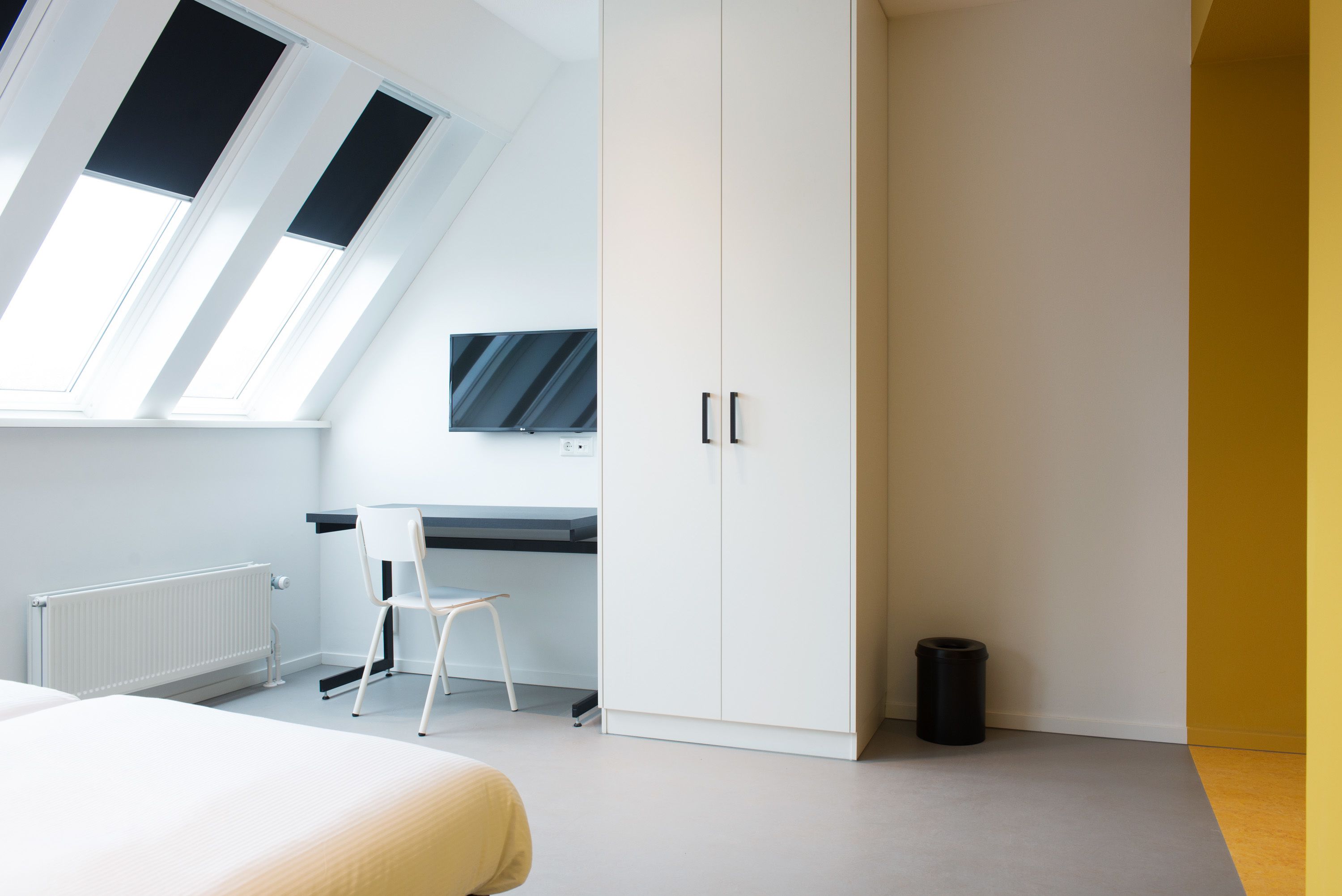 Une chambre moderne avec une lucarne, un lit, un bureau et une armoire.