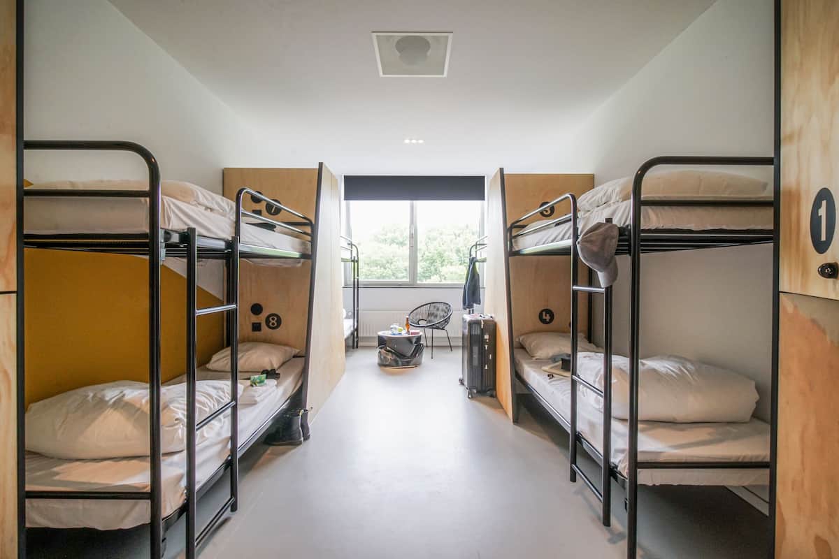 A dormitory room with bunk beds, a window, and a small seating area.