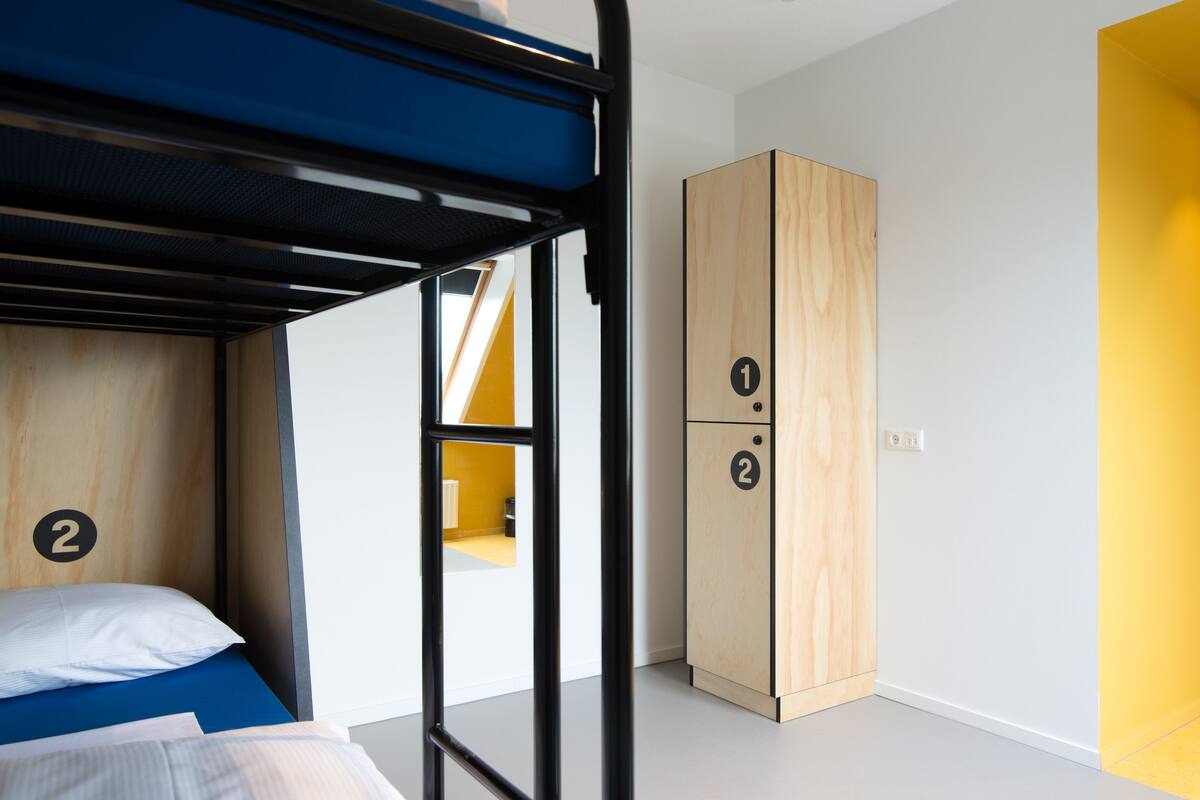 A bunk bed with a blue mattress, a wooden wardrobe with two doors, and a yellow wall.