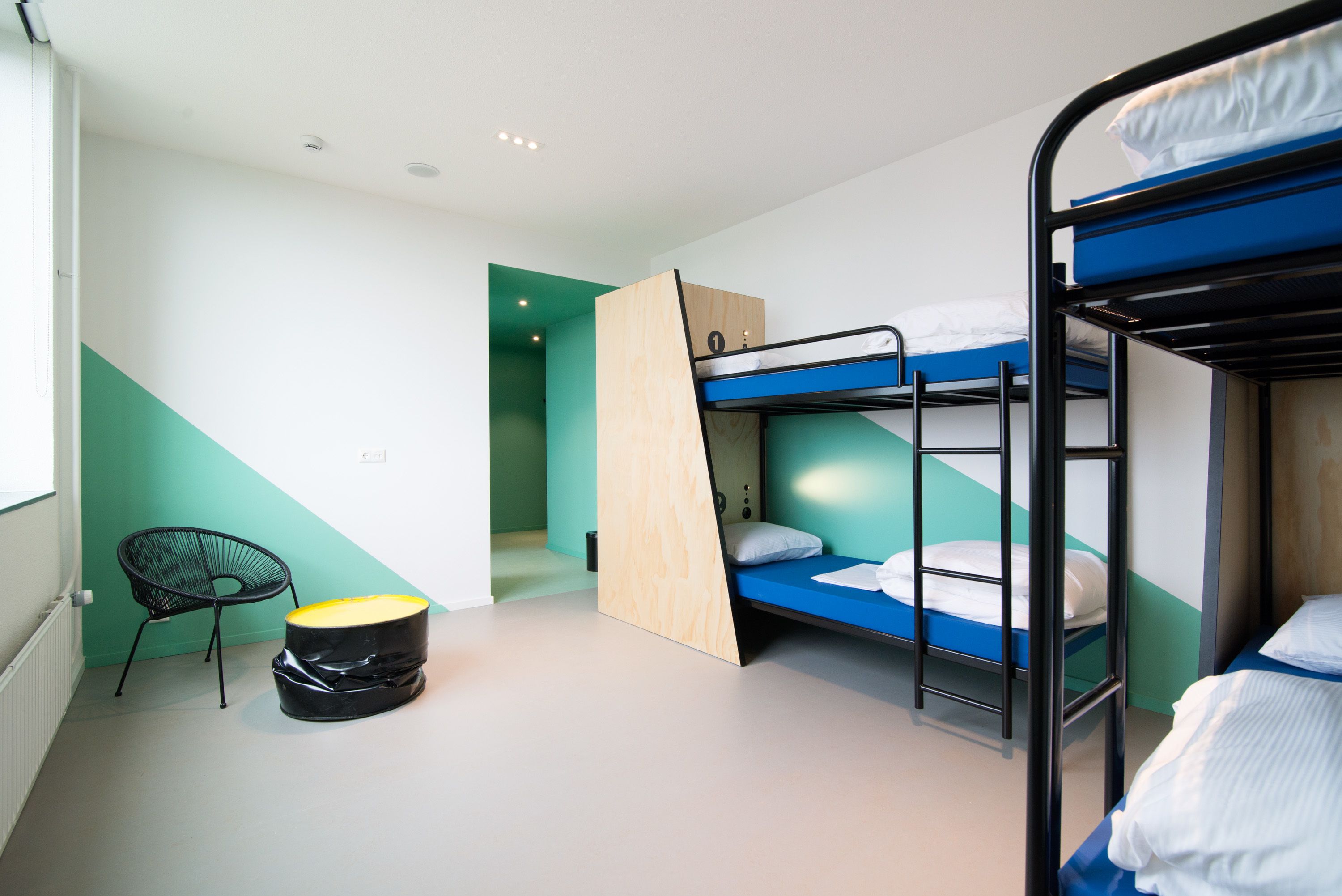 A dormitory room with bunk beds, a chair, and a small table.