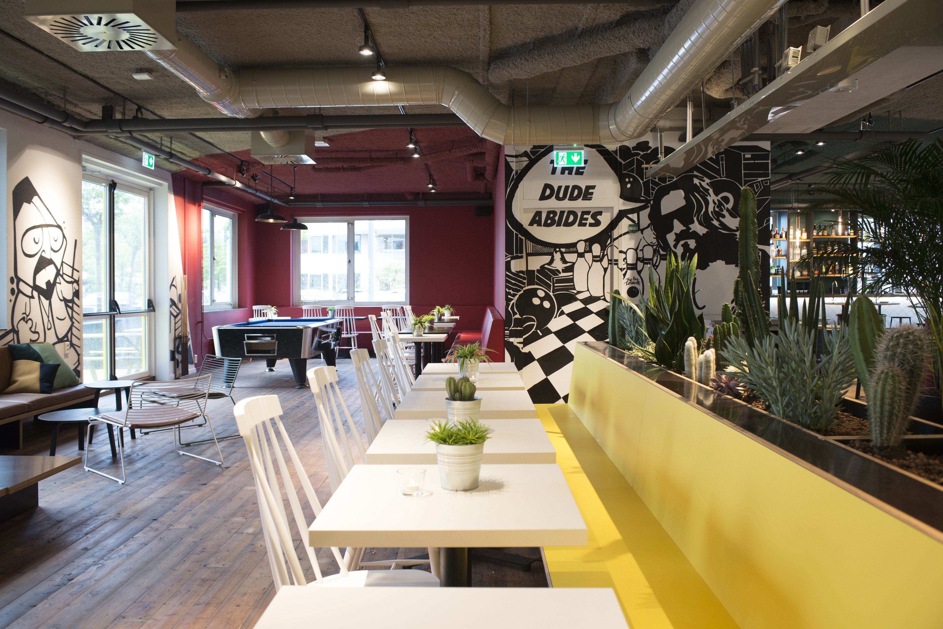 A restaurant with white tables and chairs, a pool table, and a mural on the wall.