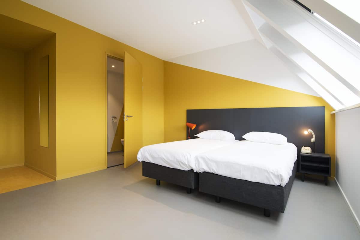 A modern bedroom with a skylight, a large bed with white linens, and a nightstand with a lamp.