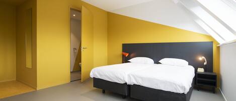 Un dormitorio moderno con tragaluces, una cama grande con ropa de cama blanca y una mesita de noche con lámpara.