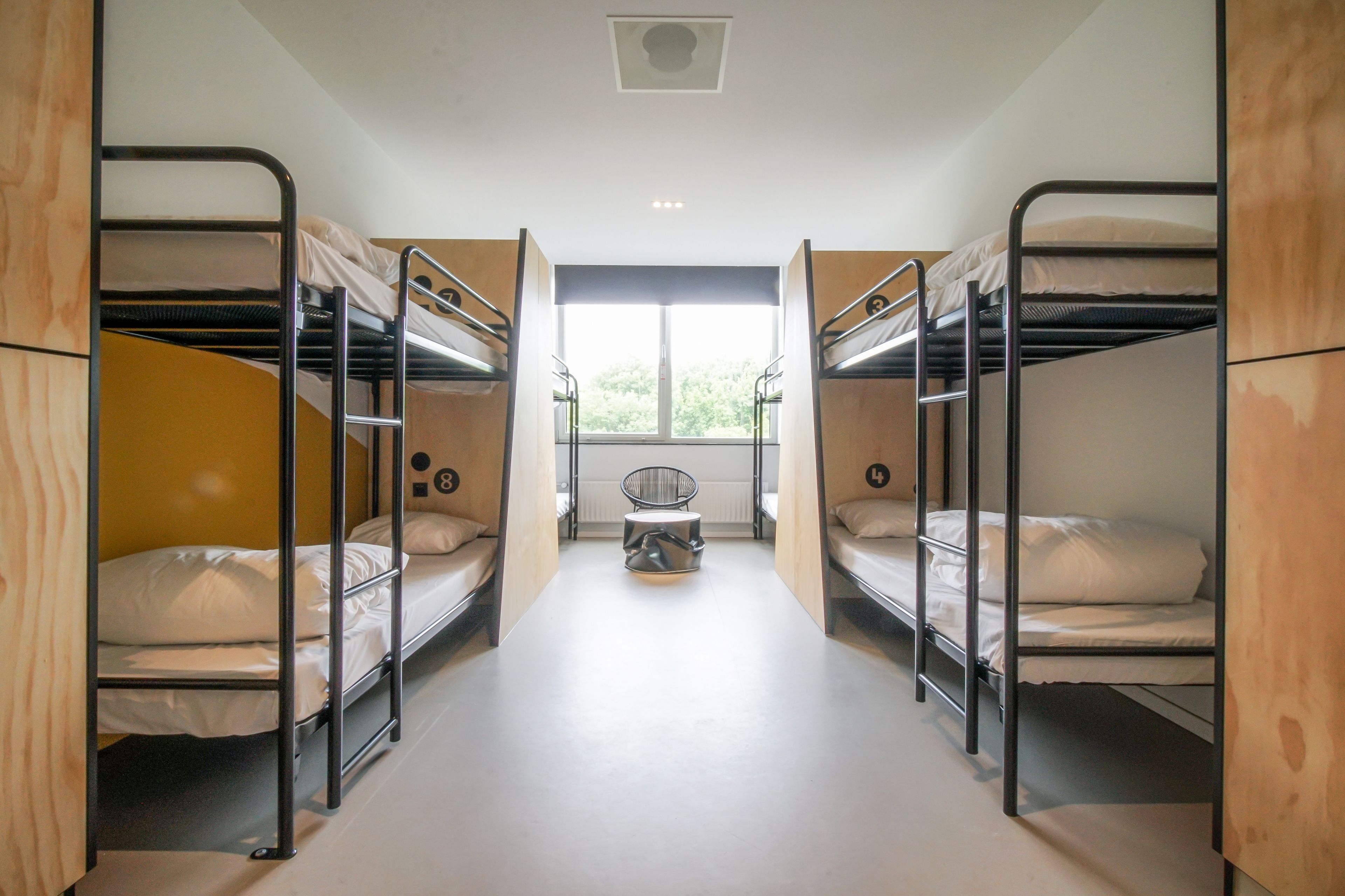 A dormitory room with bunk beds, a small stool, and a window providing natural light.