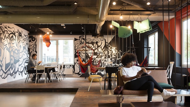 An indoor space with a wooden floor, a mural on the wall, and a seating area with a couch and chairs. - Via Amsterdam - Hostel (Diemen)