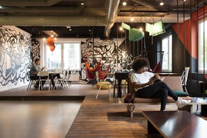 Un espacio interior con piso de madera, un mural en la pared y una zona de estar con sofá y sillones.