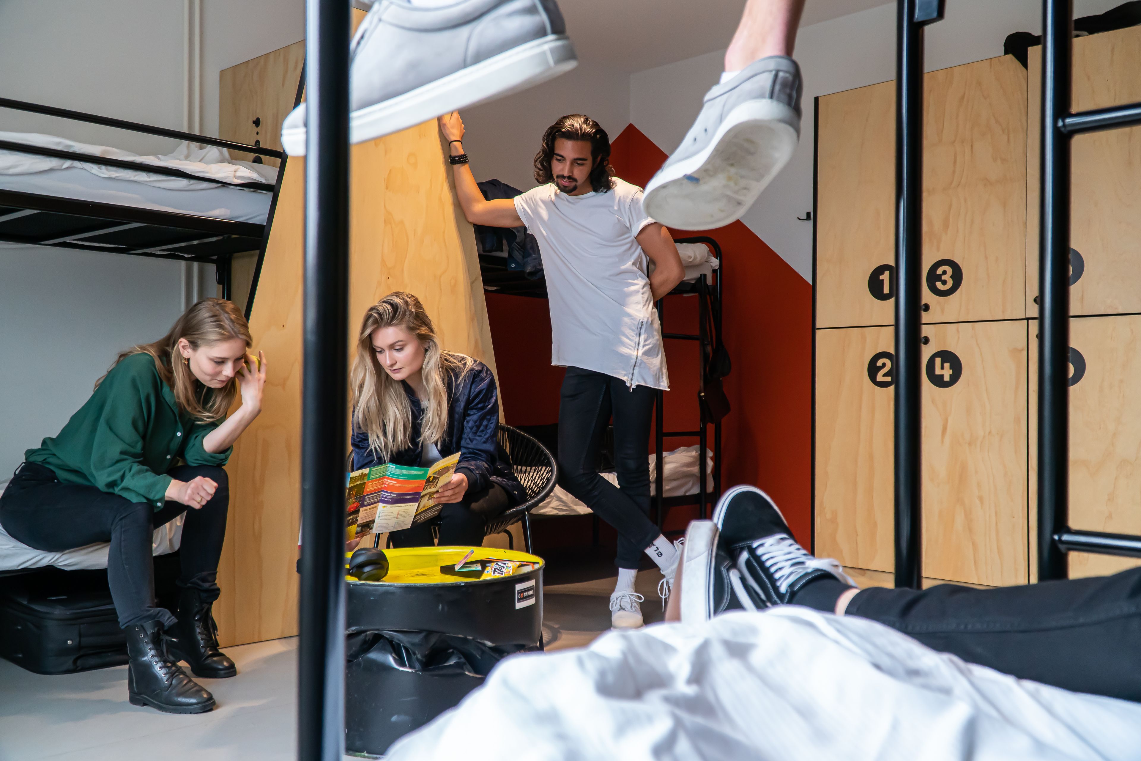 Une chambre de dortoir avec des lits superposés, une armoire en bois et une poubelle noire.