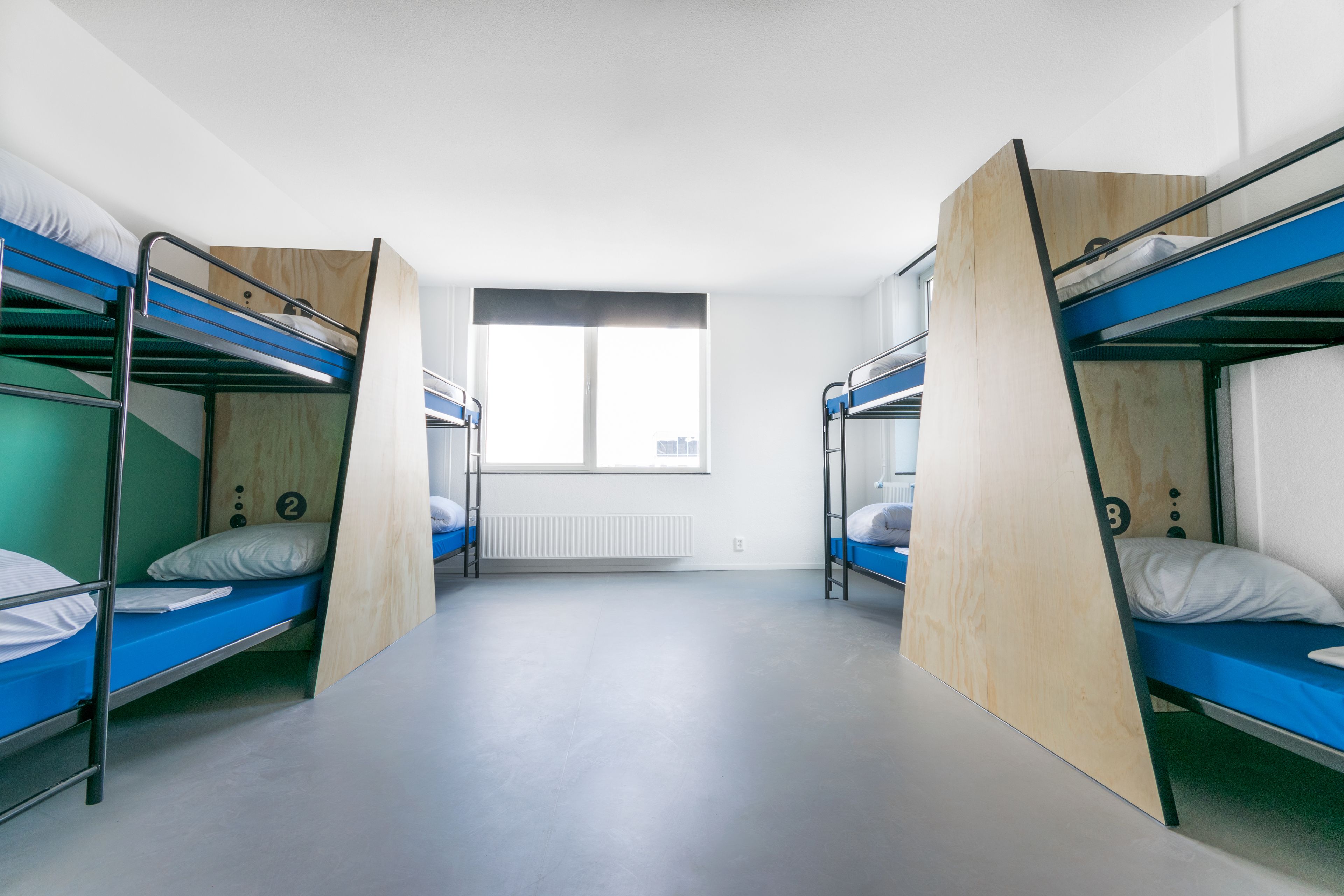 Une chambre de dortoir avec des lits superposés, une fenêtre et un radiateur.