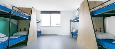 Une chambre de dortoir avec des lits superposés, une fenêtre et un radiateur.