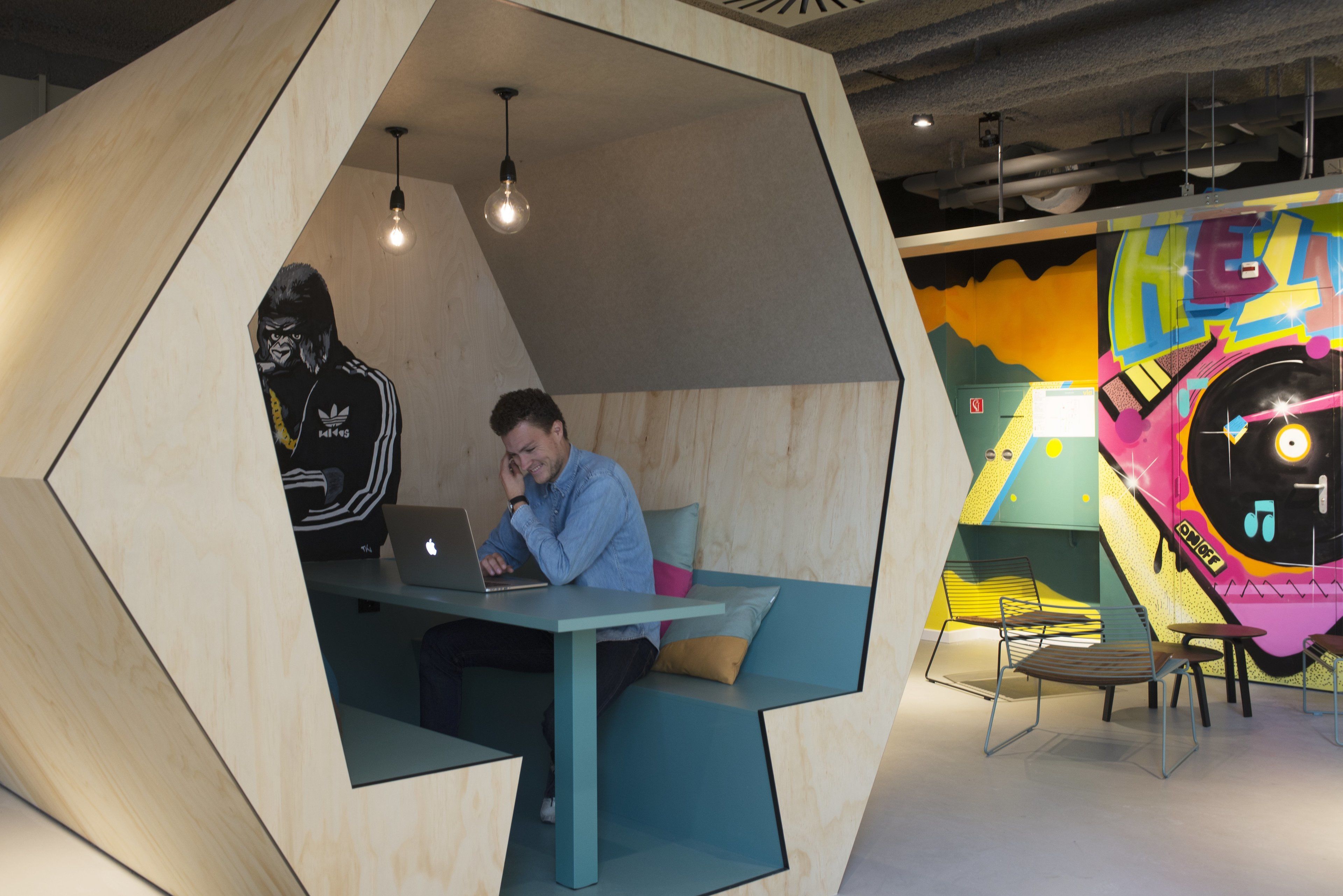 A modern, geometric-designed room with a wooden interior, a laptop on a table, and a colorful mural on the wall.