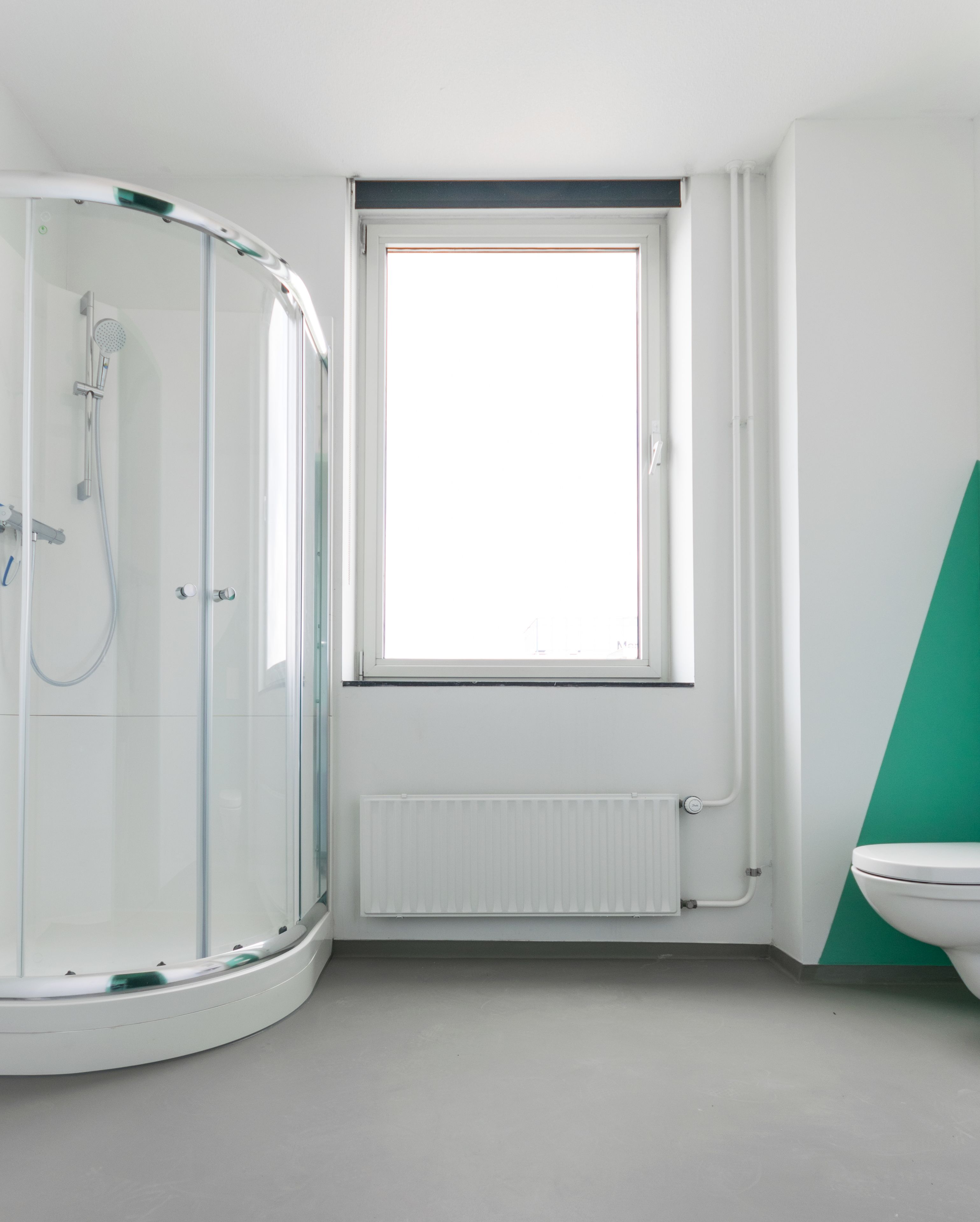 Un baño moderno con cabina de ducha de vidrio, inodoro blanco y ventana que proporciona luz natural.