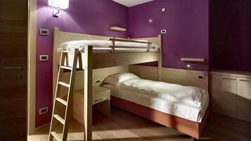 A bunk bed room with a ladder, wooden desk, and purple walls.