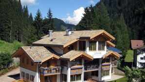 A multi-story chalet with a sloped roof, wooden balconies, and a stone pathway leading to the entrance. - Color Home Suite Apartments (Predazzo)