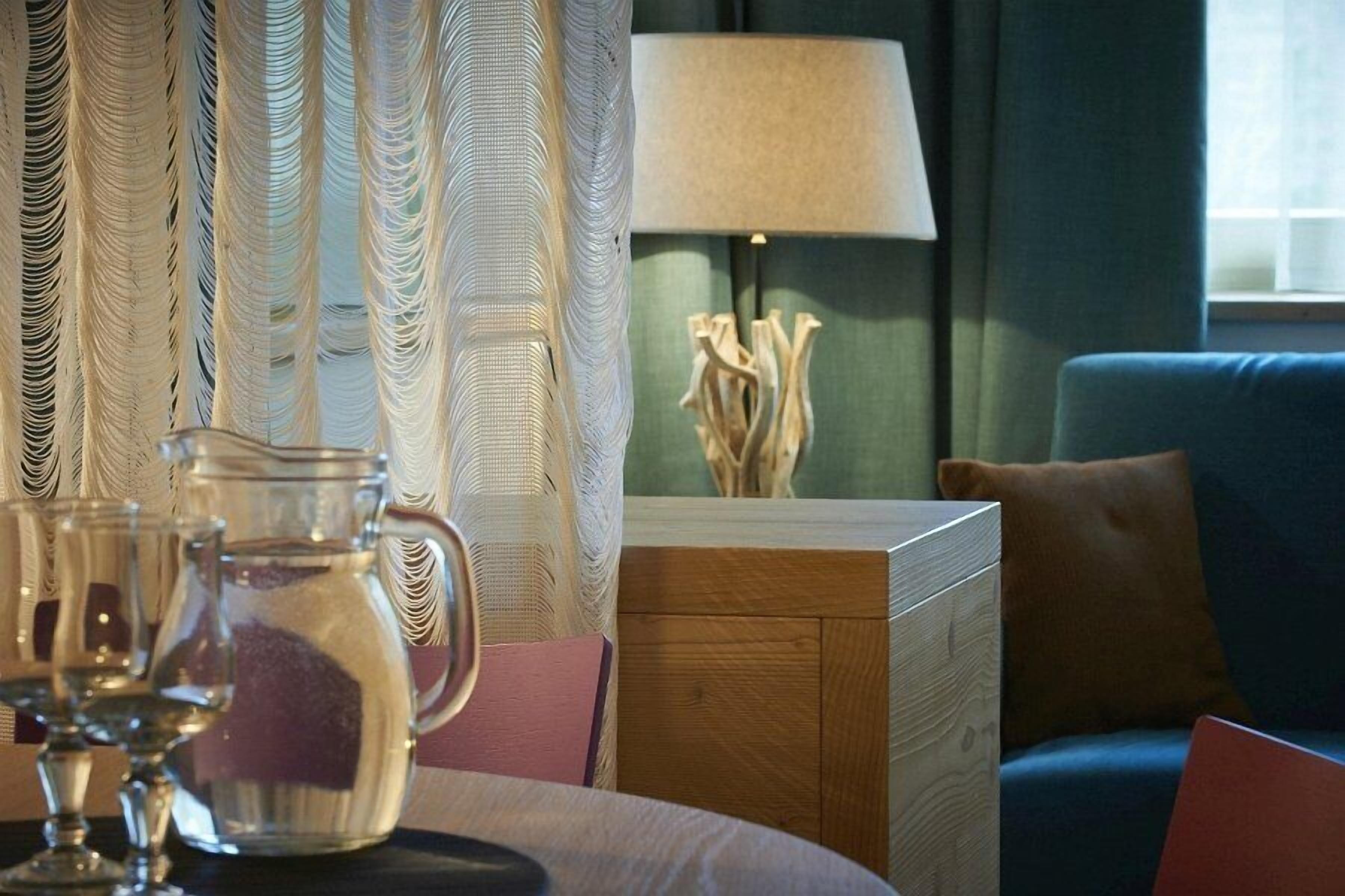 Een kamer met een houten nachtkastje, een lamp, een glazen kan en een blauwe bank.