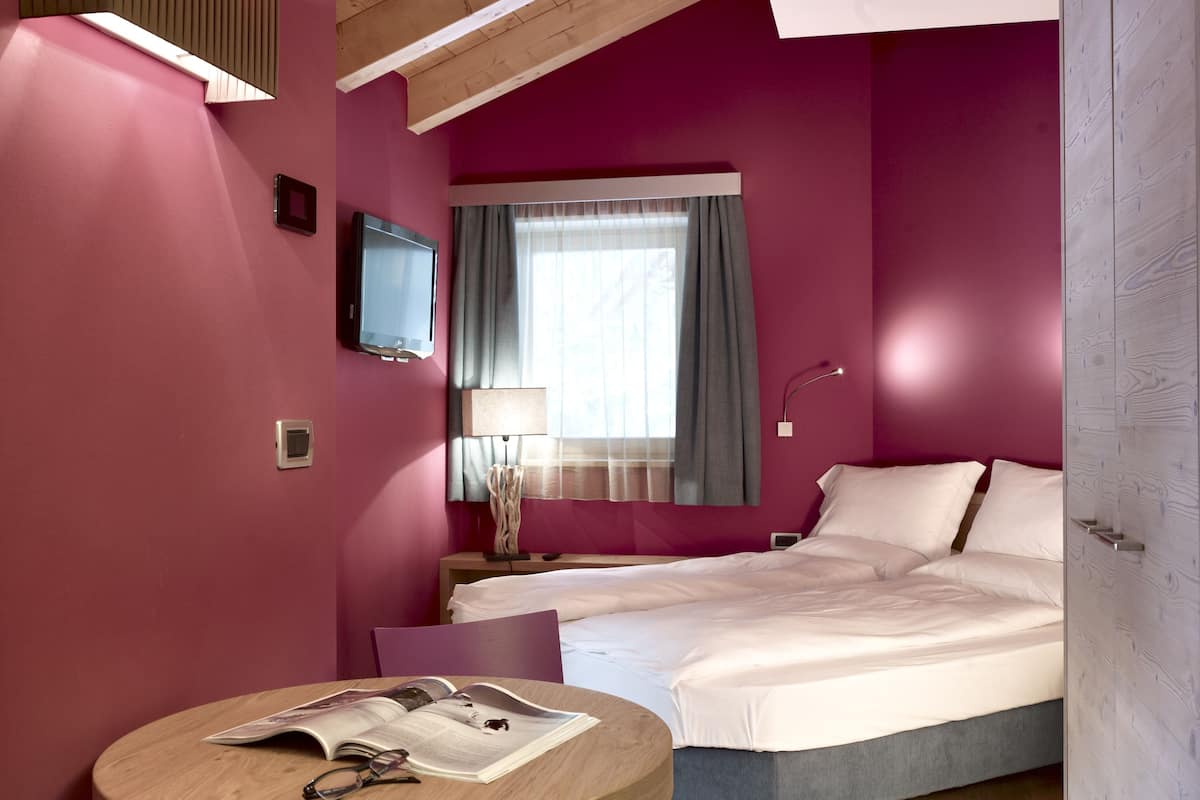 A modern hotel room with a bed, a round table with a chair, a television, and a window with curtains.