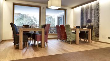 A modern dining area with wooden tables and chairs, large windows with a view of trees, and a textured wall mural.
