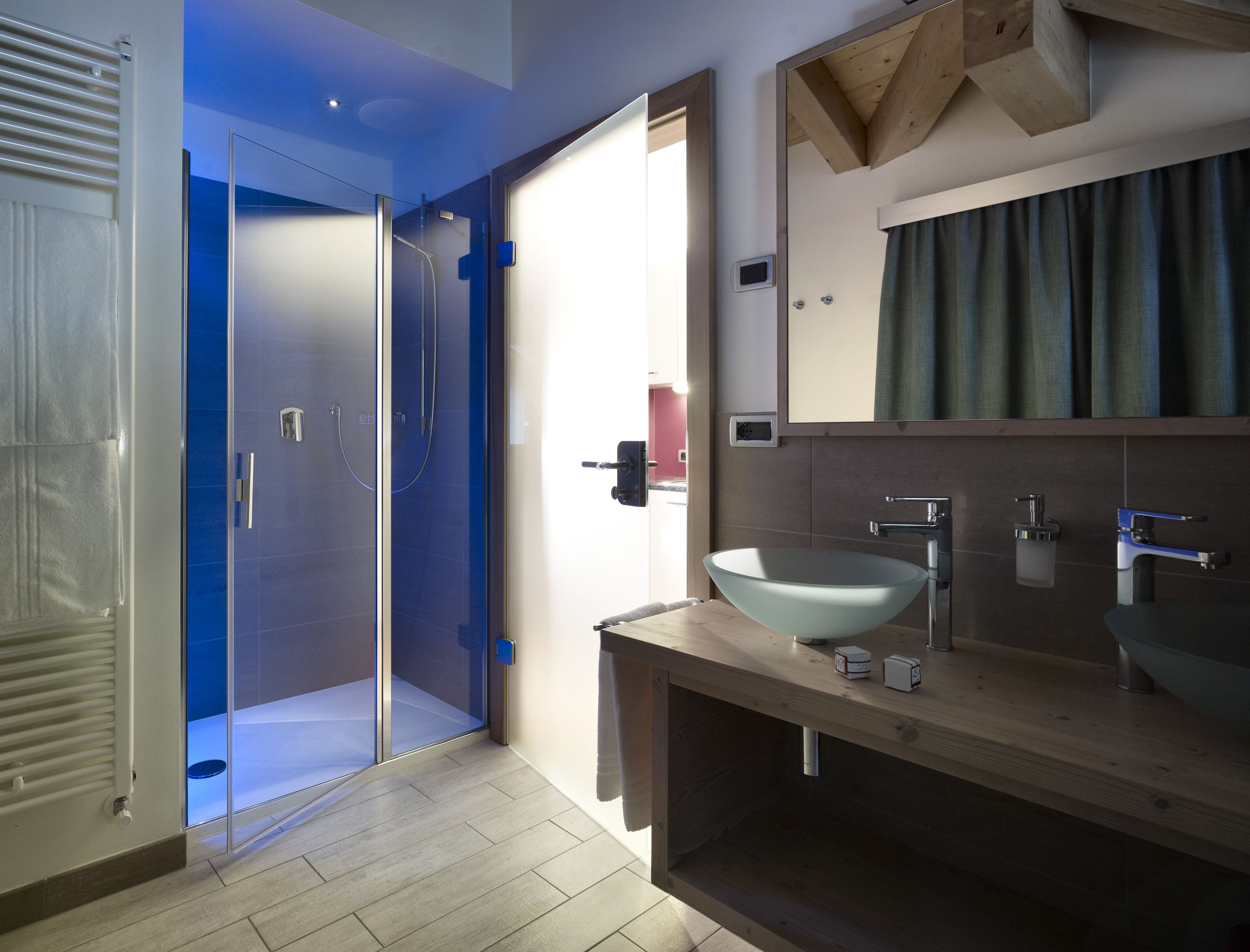 A modern bathroom with a glass-enclosed shower, a wooden vanity with a bowl sink, and a large mirror.