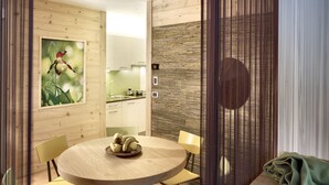 A dining area with a round table, chairs, and a fruit bowl. There is a kitchen in the background with cabinets and a sink. - Color Home Suite Apartments (Predazzo)