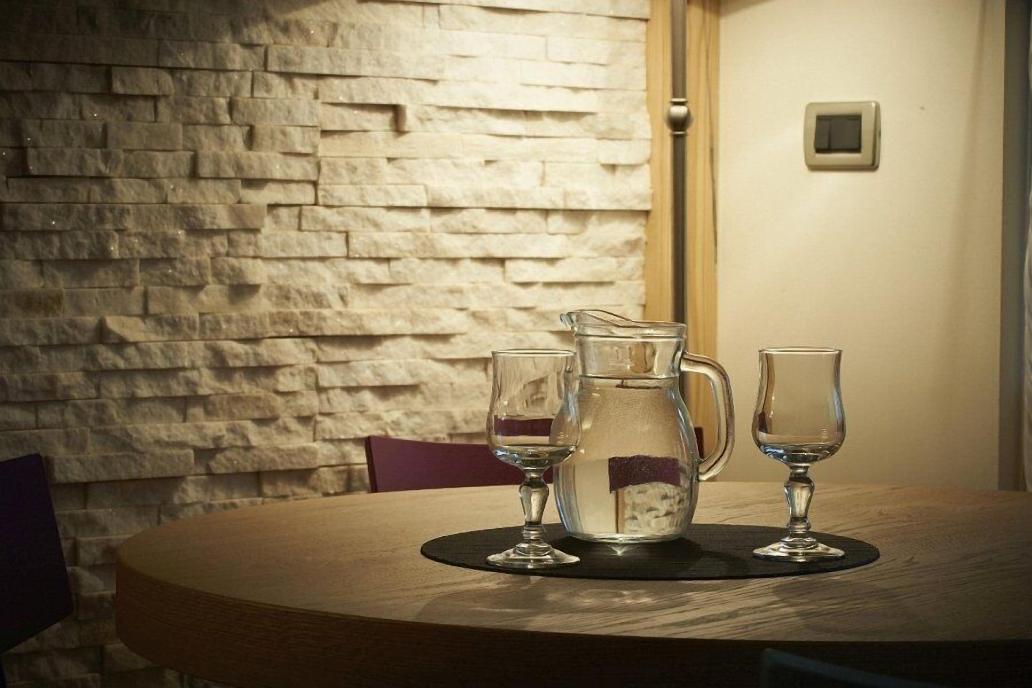 Una mesa redonda con una jarrón y dos vasos sobre un posavasos, frente a un muro de piedra.