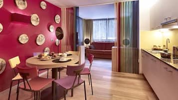 A modern living room with a round dining table, pink chairs, and a red accent wall with wooden signs.