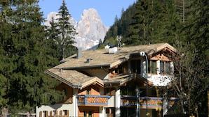 A chalet-style building with a sloped roof, wooden balconies, and a mountain backdrop. - Color Home Suite Apartments (Predazzo)