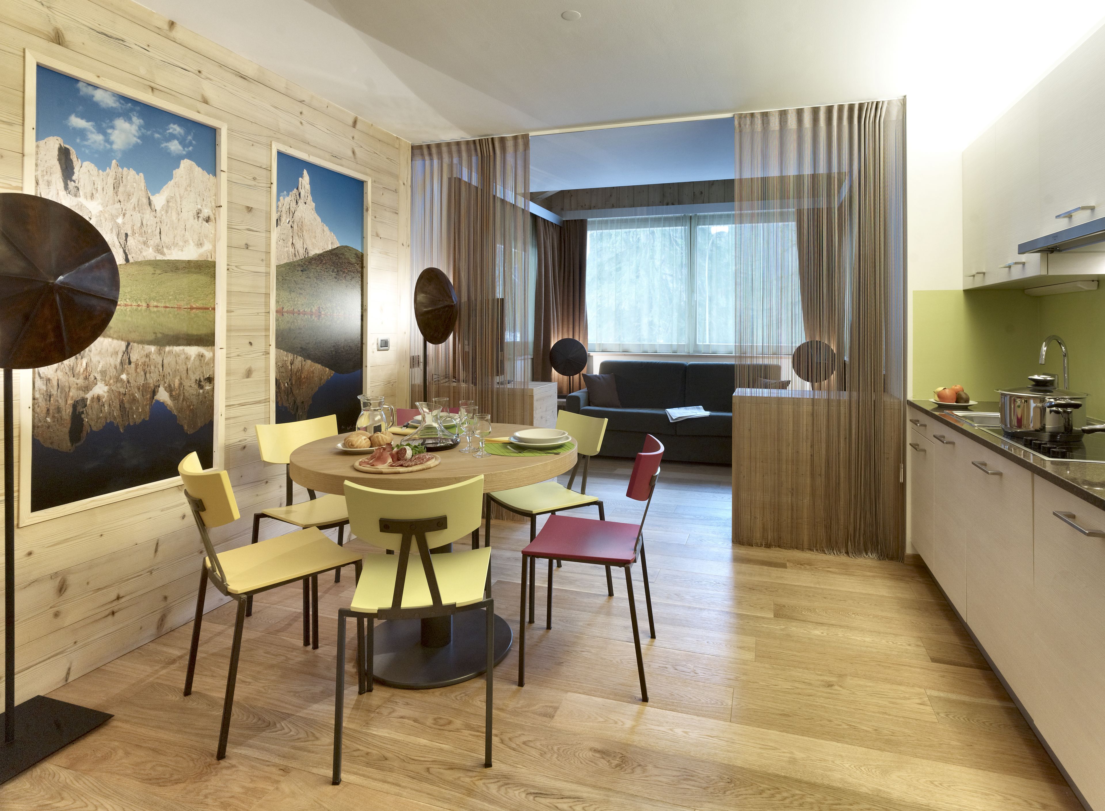 A modern kitchen with a dining area, wooden walls, and a view of the mountains.