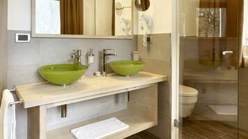 Un baño con dos lavamanos de vidrio verde, un espejo, un secador de pelo y un perchero para toallas.