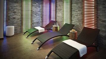 Una stanza spa con tre poltrone reclinabili, uno sgabello di legno e un lettino per massaggi.
