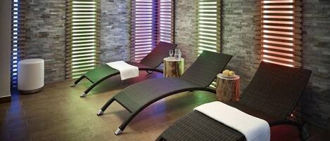 A spa room with three reclining chairs, a wooden stool, and a massage table.