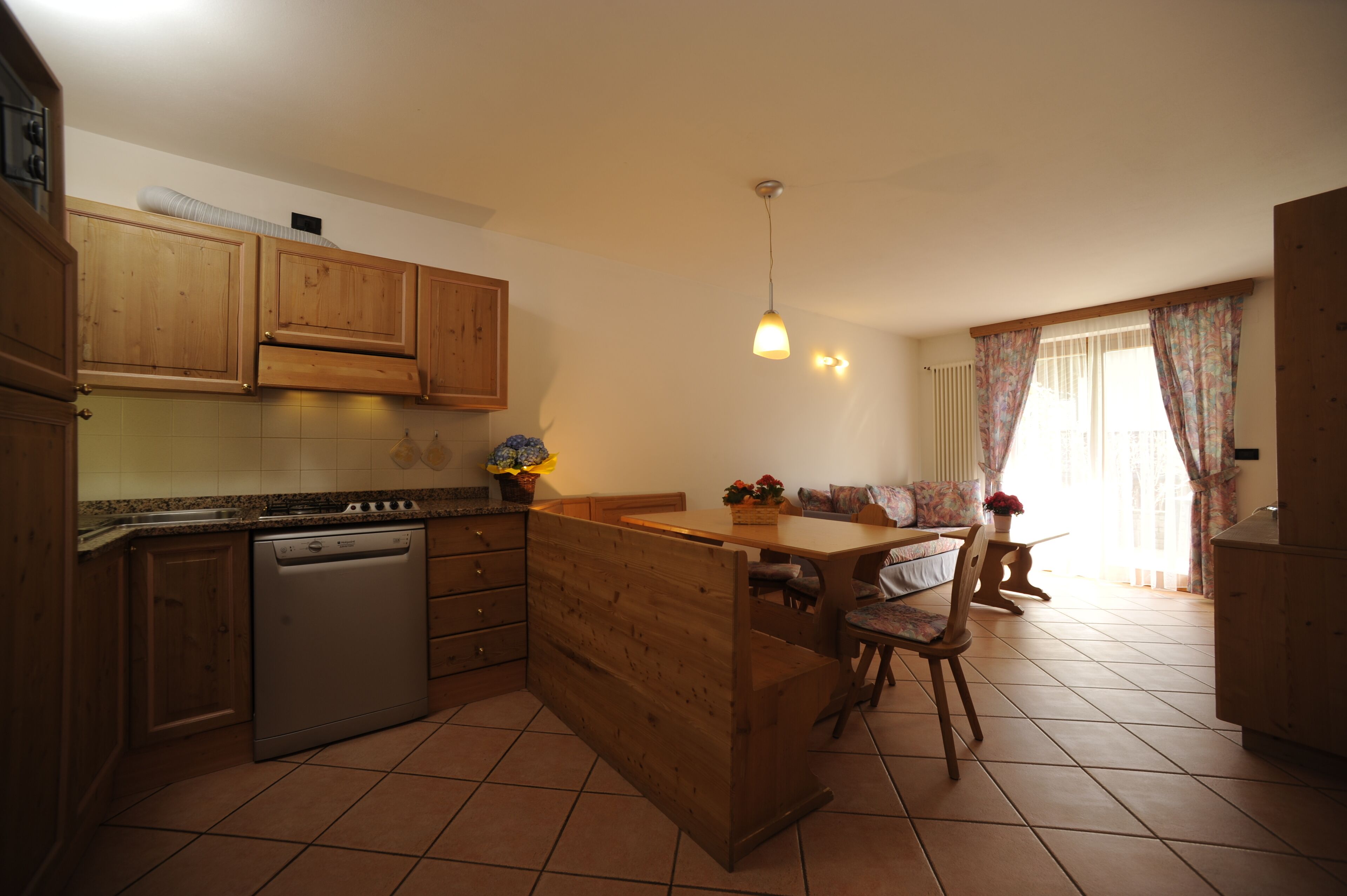 A kitchen with wooden cabinets, a dishwasher, a dining table with chairs, and a pendant light.