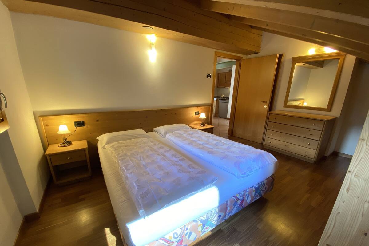 A bedroom with a wooden headboard, two bedside tables with lamps, a large bed with a patterned bedspread, a dresser, and a mirror.